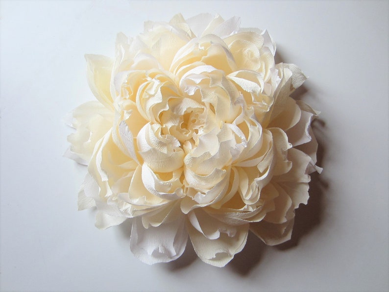 Pu&ograve; includere: Un grande fiore di carta color crema con molti strati di petali.