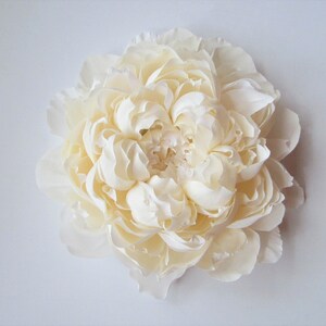 Pu&ograve; includere: Un grande fiore di seta bianco che ricorda una peonia. Il fiore ha molti strati di petali ed &egrave; disposto in forma circolare.