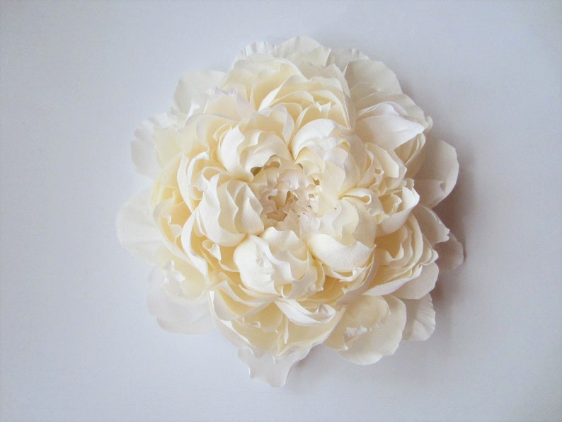 Pu&ograve; includere: Un grande fiore di seta bianco che ricorda una peonia. Il fiore ha molti strati di petali ed &egrave; disposto in forma circolare.