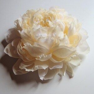 Pu&ograve; includere: Un grande fiore di carta color crema che ricorda una peonia. Il fiore &egrave; composto da molti strati di delicati petali di carta.