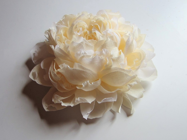 Pu&ograve; includere: Un grande fiore di carta color crema che ricorda una peonia. Il fiore &egrave; composto da molti strati di delicati petali di carta.