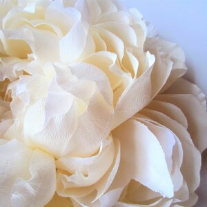Pu&ograve; includere: Un grande fiore di carta color crema con molti strati di petali. Il fiore &egrave; fatto di carta delicata e stropicciata e ha un aspetto morbido e romantico.
