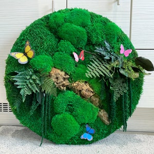 May include: A round green moss wall art piece with a variety of textures and shapes. The moss is a vibrant green and is accented with small paper butterflies in yellow, pink, and blue.