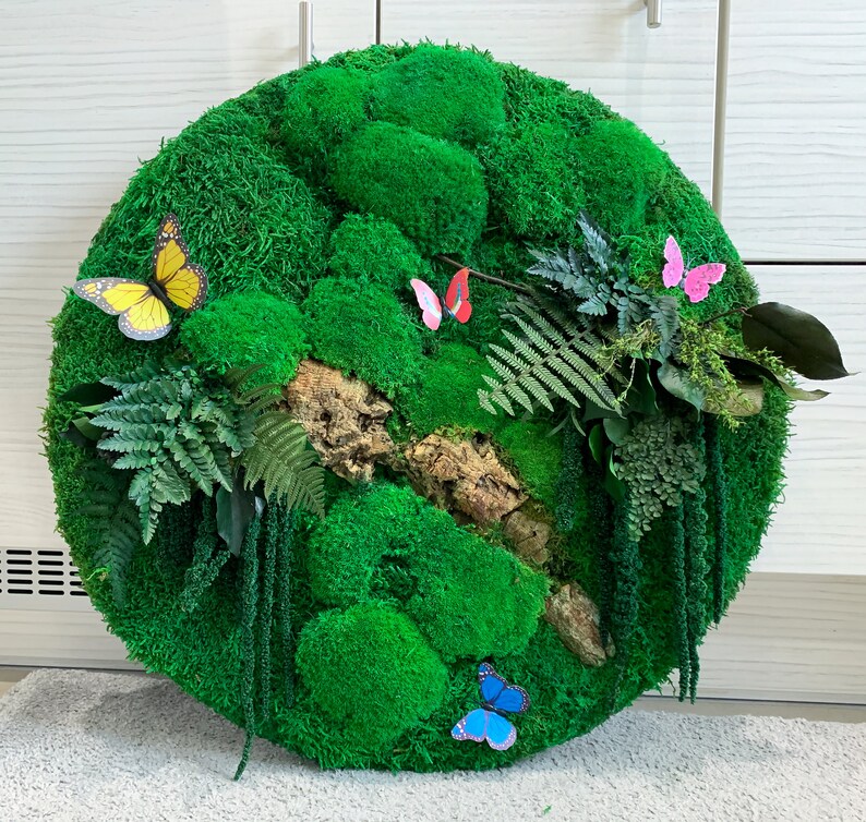 May include: A round green moss wall art piece with a variety of textures and shapes. The moss is a vibrant green and is accented with small paper butterflies in yellow, pink, and blue.