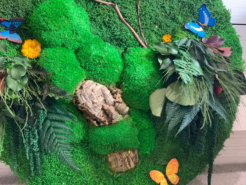May include: A green moss wall art piece with a variety of textures and colors. The piece features a cork bark, a fern, and several butterflies.