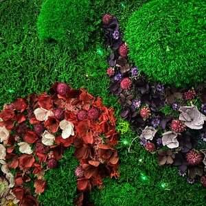 May include: A green moss wall art piece with dried flowers and petals in shades of red, pink, purple, and white. The flowers are arranged in a flowing pattern, creating a natural and organic look.