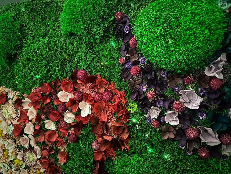 May include: A green moss wall art piece with dried flowers and petals in shades of red, pink, purple, and white. The flowers are arranged in a flowing pattern, creating a natural and organic look.