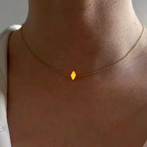 Könnte beinhalten: Eine zarte goldene Halskette mit einem kleinen, leuchtend gelben rautenförmigen Anhänger. Die Kette ist fein und liegt anmutig am Hals. Der Anhänger ist der Blickfang und verleiht einen Hauch von subtiler Eleganz.
