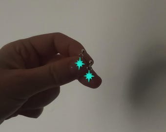 May include: A pair of silver earrings with a glow-in-the-dark star charm. The stars are a bright green color.