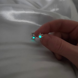 May include: A pair of silver star-shaped earrings with a green glow-in-the-dark center.