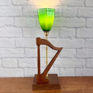 May include: A wooden harp lamp with a green glass shade. The harp is made of dark wood and has a gold metal base. The lamp is on a wooden table.