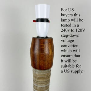 May include: A lamp component featuring a white plastic socket with a small red switch, mounted atop a polished brown wooden cylindrical base, which sits on a textured, light-colored, ribbed column. Text regarding voltage conversion is visible.