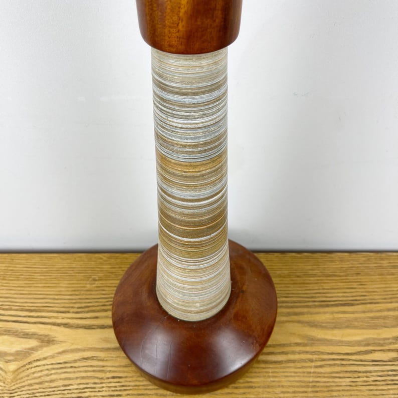May include: A table lamp base featuring a smooth, dark brown wooden top and a matching circular wooden base. The central column is composed of stacked, thin horizontal layers in alternating shades of white, gray, and light brown, creating a textured, striped appearance.