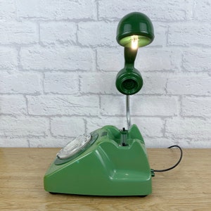 May include: A green rotary phone with a green lamp attached to the handset. The lamp has a light bulb that is turned on.