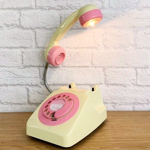 A quirky lamp made from a retro phone. The base of the lamp is a classic cream rotary phone with a pink dial & dial ring. The cream handset mounted on a flexible gooseneck has a small LED bulb in the receiver converting it into a fabulous lamp.