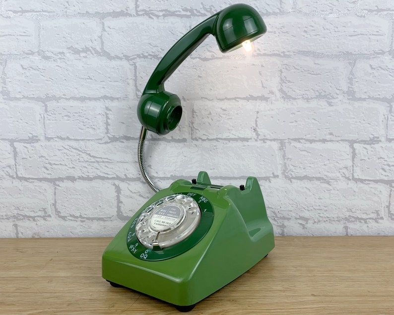 May include: A green rotary phone with a built-in lamp. The phone has a green dial with white numbers and a white 'Call Meter' label. The lamp is attached to the phone's handset and has a green shade.