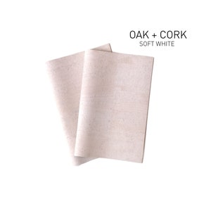 Könnte beinhalten: Zwei Blätter aus cremefarbenem Kork- und Eichenmaterial, in der Mitte gefaltet. Der Text "OAK + CORK SOFT WHITE" ist über dem Material gedruckt.