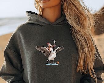 Puede incluir: Una sudadera con capucha gris oscuro con un gráfico de un oso con un gorro rojo montando un ganso que sostiene un palo de hockey. El ganso está volando con las alas extendidas.