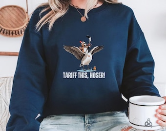 Puede incluir: Una sudadera azul marino con un gráfico de un ganso de dibujos animados que lleva un gorro de Papá Noel y sostiene un palo de hockey. El texto "Tariff This, Hoser!" está impreso debajo del gráfico.