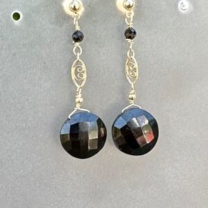 May include: A pair of dangle earrings featuring black faceted gemstones and gold filigree accents.