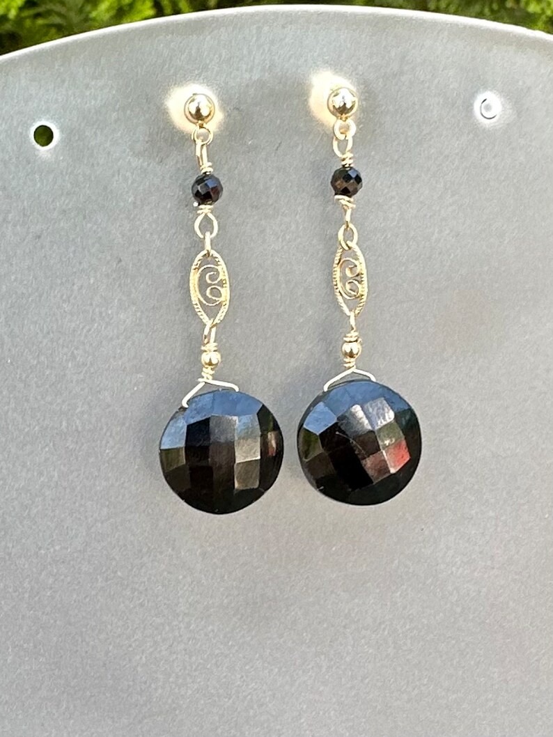 May include: A pair of dangle earrings featuring black faceted gemstones and gold filigree accents.