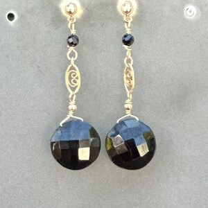 May include: A pair of gold earrings featuring black faceted gemstones and a delicate gold chain design.