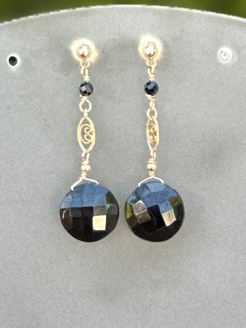 May include: A pair of gold earrings featuring black faceted gemstones and a delicate gold chain design.