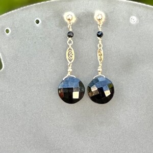 May include: A pair of dangle earrings featuring black faceted gemstones and a gold filigree design.