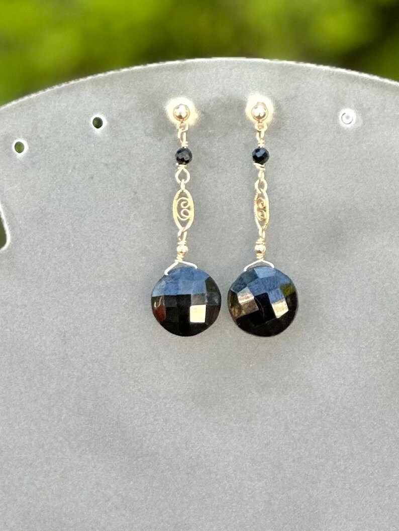 May include: A pair of dangle earrings featuring black faceted gemstones and a gold filigree design.