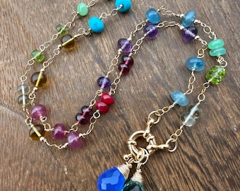 Puede incluir: Un collar de cadena de oro con una variedad de cuentas de piedras preciosas de colores, incluyendo turquesa, amatista, aguamarina y peridoto. El collar tiene un cierre de oro y dos colgantes de piedra preciosa en forma de lágrima.