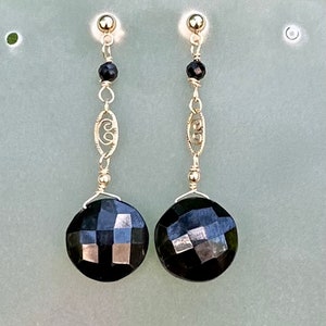 May include: A pair of gold earrings featuring black faceted gemstones and a delicate gold chain design.
