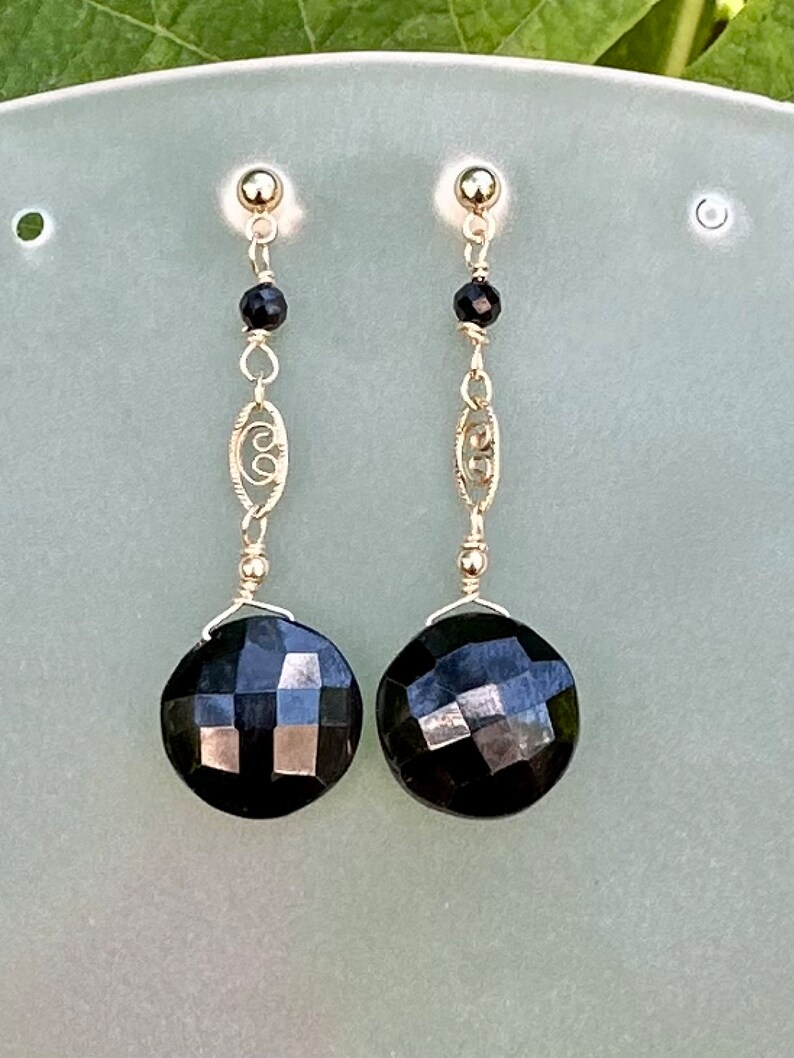 May include: A pair of gold earrings featuring black faceted gemstones and a delicate gold chain design.