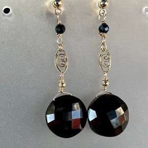 May include: A pair of dangle earrings featuring black faceted stones and gold filigree accents.