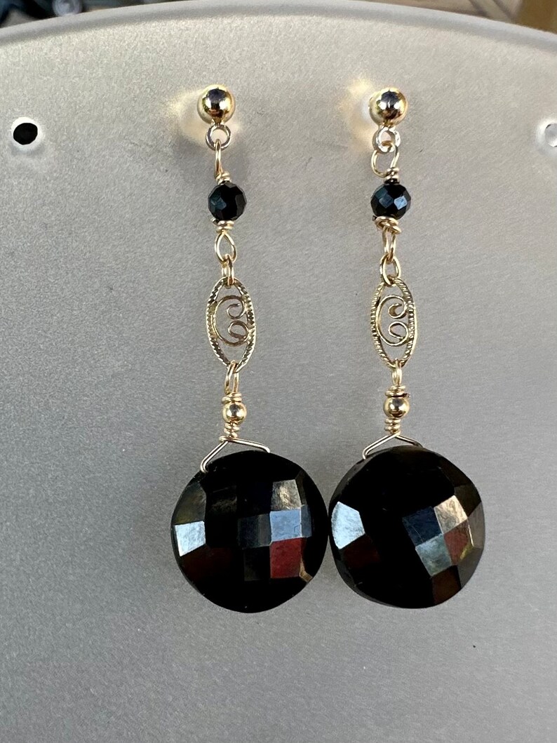 May include: A pair of dangle earrings featuring black faceted stones and gold filigree accents.