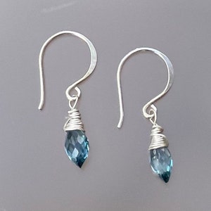 Puede incluir: Un par de pendientes de plata con piedras preciosas azules en forma de lágrima. Los pendientes están hechos de alambre envuelto alrededor de las piedras preciosas.