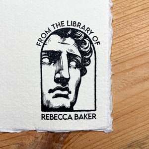 May include: Black and white illustration of a bust of a man with the text "From the Library of Rebecca Baker" around the bust.