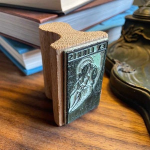 Pu&ograve; includere: Un timbro per libri in legno con un'immagine verde e bianca di una donna che tiene un libro. Il timbro recita "Ex Libris".