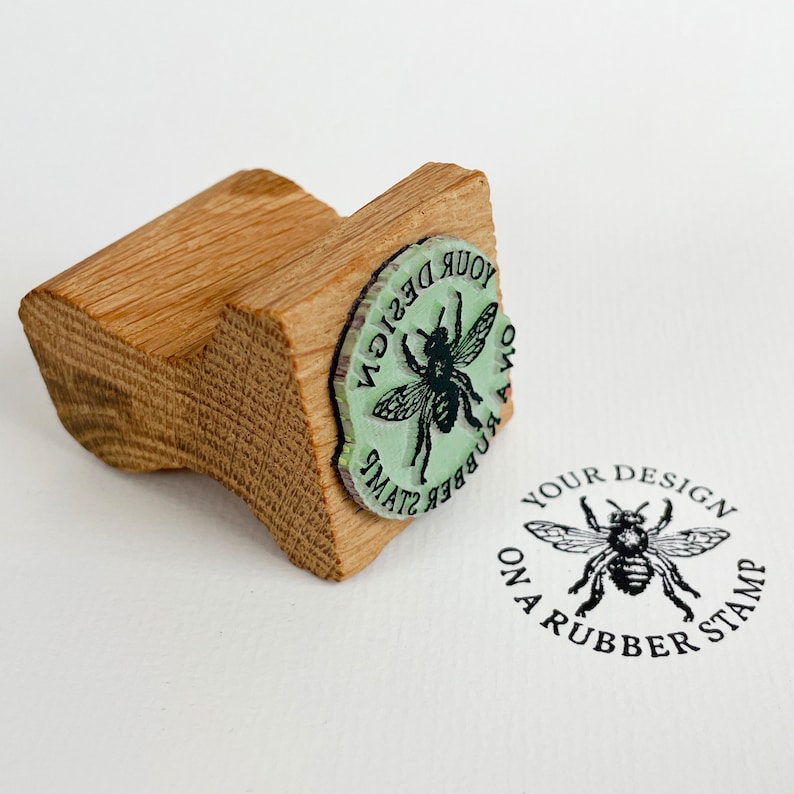 Pu&ograve; includere: Un timbro di legno con un design di ape. Il timbro recita "Your design on a rubber stamp".