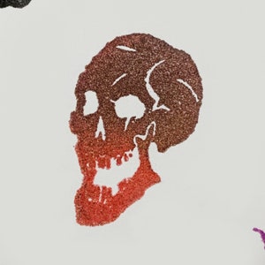 Pu&ograve; includere: Un design a teschio glitterato nei toni del rosso e del marrone, con effetto sfumato. Il teschio &egrave; una grafica a tema Halloween o gotico, adatta per abbigliamento o decorazioni.