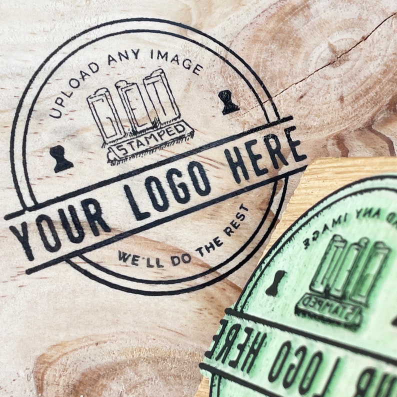 Pu&ograve; includere: Un timbro circolare in bianco e nero con il testo "UPLOAD ANY IMAGE GET IT STAMPED YOUR LOGO HERE WE'LL DO THE REST" su una superficie di legno.