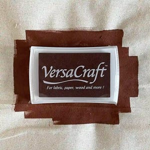 May include: A brown ink pad with the text "VersaCraft" and the words "For fabric, paper, wood and more!" in white.