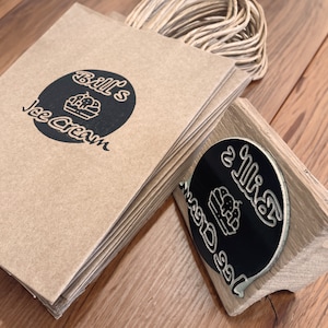 Pu&ograve; includere: Una pila di sacchetti di carta marrone con un logo in bianco e nero che dice "Bill's Ice Cream" e un timbro di gomma in bianco e nero con lo stesso logo.