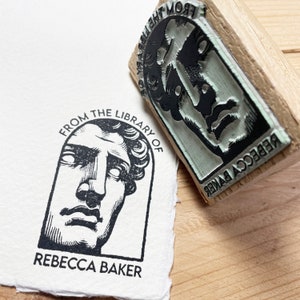 May include: A black and white rubber stamp with the text "From the Library of Rebecca Baker" and a drawing of a person's face.