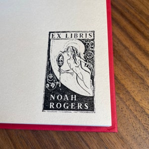 Pu&ograve; includere: Ex libris in bianco e nero con una donna che tiene uno specchio con un teschio al suo interno. Il testo "Ex Libris Noah Rogers" &egrave; sotto l'immagine.