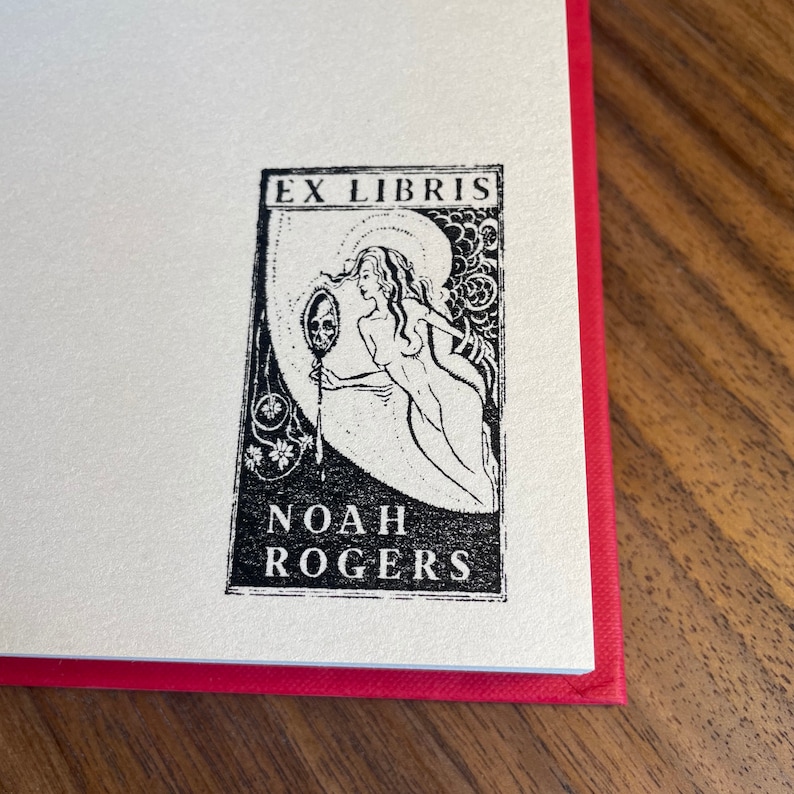 Pu&ograve; includere: Ex libris in bianco e nero con una donna che tiene uno specchio con un teschio al suo interno. Il testo "Ex Libris Noah Rogers" &egrave; sotto l'immagine.