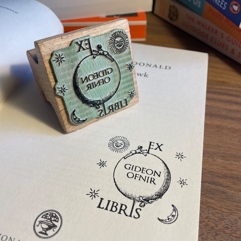 May include: A wooden stamp with a green and black design. The stamp features a globe with the text "Gideon Ofnir" and "Libris" around it. There are stars and a sun on the stamp.