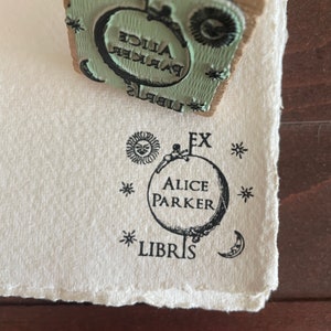 May include: A black and white stamp with the text "Ex Libris Alice Parker" and a small figure holding onto a globe. The globe has stars and a crescent moon around it.