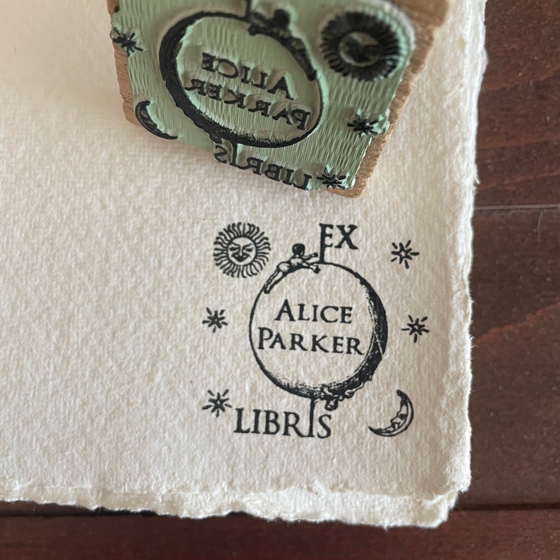 May include: A black and white stamp with the text "Ex Libris Alice Parker" and a small figure holding onto a globe. The globe has stars and a crescent moon around it.