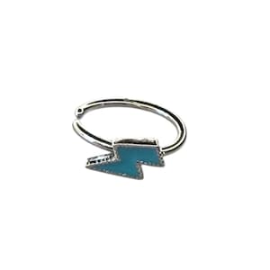 May include: A silver nose ring with a turquoise lightning bolt charm. The lightning bolt is a vibrant turquoise colour and is attached to a simple, circular ring, perfect for a nose piercing.
