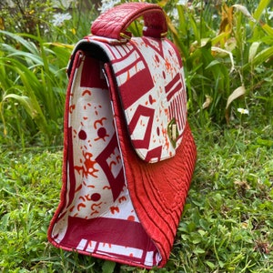 May include: A red leather handbag with a white and red patterned flap. The bag has a top handle and a gold clasp.
